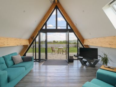 A living room with teal sofas a television and a glass door opening to a patio with chairs at Kerry Hill - The Sheepfold in Llanyre near Llandrindod Wells