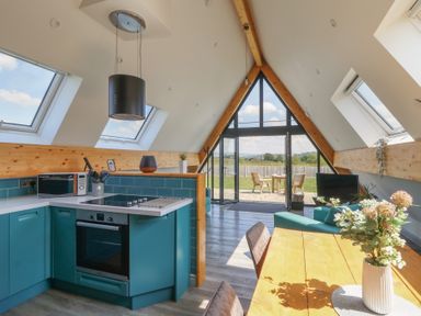 A kitchen and living area with teal cabinets wooden table and large triangular windows at Kerry Hill The Sheepfold Llanyre near Llandrindod Wells