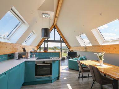 A kitchen and dining area with teal cabinets a wooden table and a sitting area with a teal sofa in an attic space at Kerry Hill The Sheepfold Llanyre near Llandrindod Wells