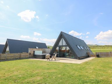 A triangular house with glass windows patio furniture and a hot tub in a fenced yard at Kerry Hill - The Sheepfold in Llanyre near Llandrindod Wells