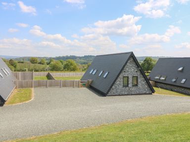 Three stone and slate roof houses with fenced yards and gravel driveway in a rural hilly landscape at Kerry Hill - The Sheepfold in Llanyre near Llandrindod Wells