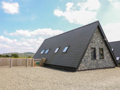 A stone and slate roof triangular house with multiple skylights and a wooden fence at Kerry Hill - The Sheepfold in Llanyre near Llandrindod Wells