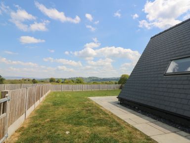 A fenced grass yard with a paved pathway next to a building with slate siding at Kerry Hill The Sheepfold in Llanyre near Llandrindod Wells