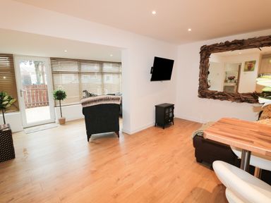 A living area with wooden floor a mounted TV a large wooden framed mirror and a door with blinds at Swale Cottage in Beadnell