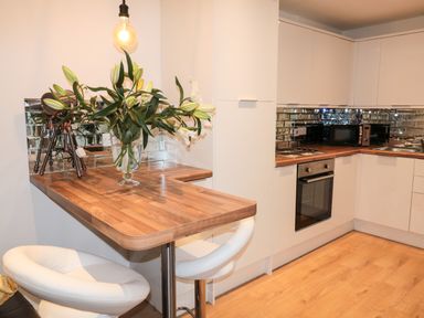 A kitchen with white cabinets a wooden countertop a vase with flowers a bar stool and an oven at Swale Cottage Beadnell