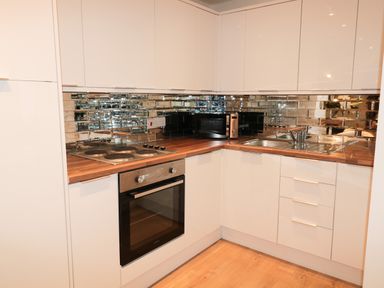 A kitchen corner with white cabinets wooden countertops an electric stove an oven a microwave a sink and a mirrored backsplash at Swale Cottage in Beadnell