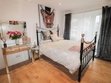 A bedroom with a bed a mirrored dressing table a vase of flowers and a colorful animal painting at Swale Cottage in Beadnell