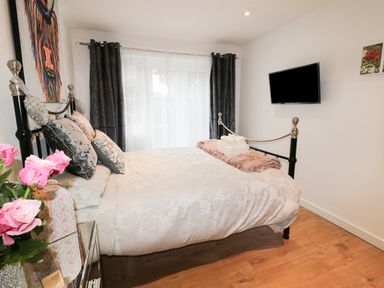 A bedroom with a metal bed frame bedding and pillows a wall-mounted television and windows with curtains at Swale Cottage in Beadnell