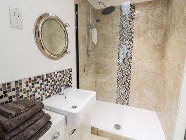 A bathroom with a sink a circular mirror a walk in shower with mosaic tiles at Swale Cottage in Beadnell