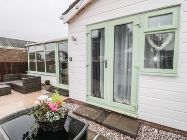 An outdoor patio area with green framed glass doors and windows with a wicker sofa and a flower pot on a wicker table at Swale Cottage in Beadnell