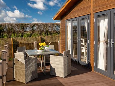 An outdoor patio with a glass table and four wicker chairs next to a house with glass doors at Lobster Lodge in Runswick Bay