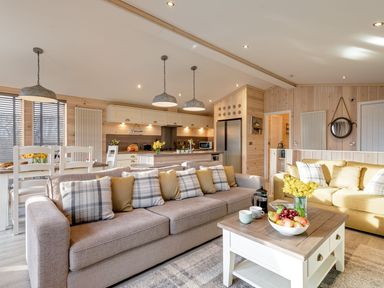 An open-plan living room and kitchen with sofas, a coffee table with fruit and flowers, dining table with chairs at Lobster Lodge in Runswick Bay