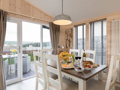 A dining area with a wooden table set with food and drinks next to glass doors and windows at Lobster Lodge in Runswick Bay