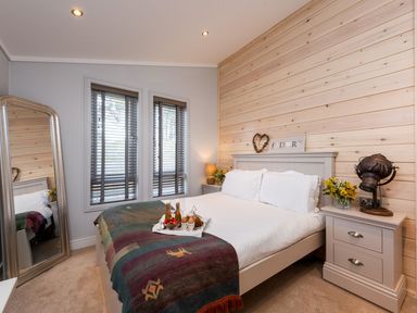 A bedroom with a bed covered by a blanket and bedside tables with flowers and a lamp at Lobster Lodge in Runswick Bay