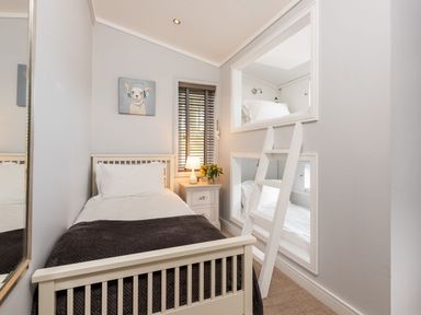 A bedroom with a single bed a bunk bed with a ladder a nightstand with a lamp and flowers and a dog painting on the wall at Lobster Lodge in Runswick Bay