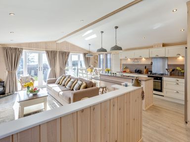 An open plan kitchen and living room with a sofa dining table flowers and large windows at Lobster Lodge in Runswick Bay