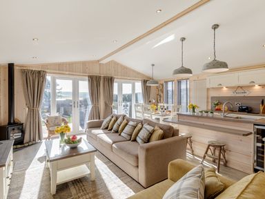 An open living area with sofas coffee table kitchen island dining table and large windows at Lobster Lodge in Runswick Bay