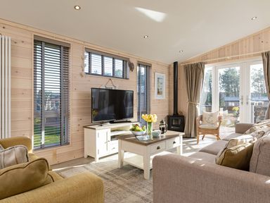 A living room with a TV on a stand a coffee table with fruit and flowers and sofas at Lobster Lodge in Runswick Bay