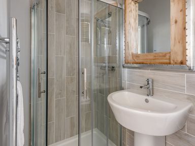 A bathroom with a glass shower enclosure a white sink a wooden framed mirror and a towel rail at Lobster Lodge in Runswick Bay