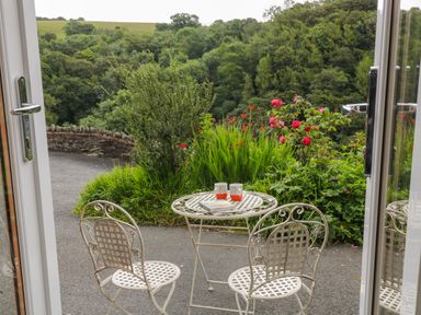 A metal table and two chairs set outside near greenery and flowers with a countryside view at Ferndale in Lynton