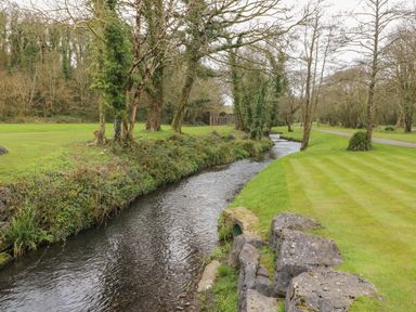 A river flowing through a park with grass and trees alongside at Cwtch Lodge 42 Stepaside near Wisemans Bridge