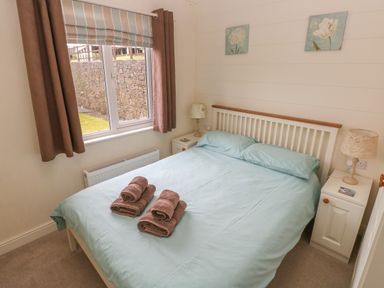 A bedroom with a double bed brown towels on the bed bedside tables and lamps at Cwtch Lodge 42 Stepaside near Wisemans Bridge