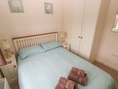 A bedroom with a double bed blue bedding bedside tables with lamps and a wardrobe at Cwtch Lodge 42 Stepaside near Wisemans Bridge