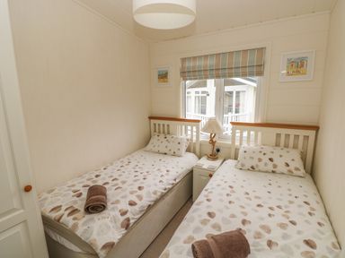 A bedroom with two single beds with heart-patterned bedding and a nightstand with a lamp between them at Cwtch Lodge 42 in Stepaside near Wisemans Bridge