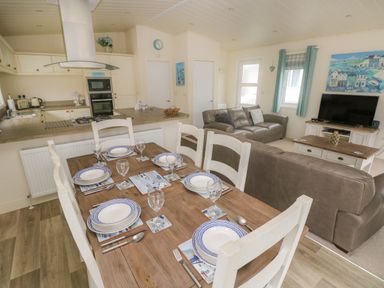 A kitchen and dining area with a wooden table set for six near a living room with leather sofas and a television at Cwtch Lodge 42 Stepaside near Wisemans Bridge