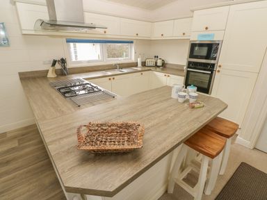 A kitchen with wooden countertops with a gas stove and stools at Cwtch Lodge 42 Stepaside near Wisemans Bridge