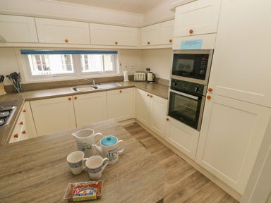 A kitchen with white cabinets wooden countertops a microwave oven a kettle toaster and mugs on a table at Cwtch Lodge 42 Stepaside near Wisemans Bridge
