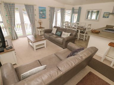 A living room with two leather sofas a coffee table a dining table and kitchen counter at Cwtch Lodge 42 Stepaside near Wisemans Bridge