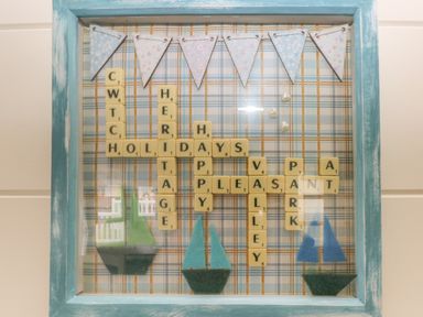 A framed decorative board with Scrabble tiles spelling words and paper sailboats at Cwtch Lodge 42 Stepaside near Wisemans Bridge
