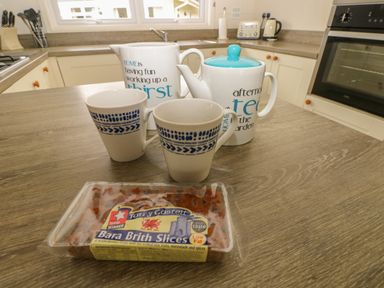 A kitchen counter with two mugs two teapots and a packaged Bara Brith cake at Cwtch Lodge 42 in Stepaside near Wisemans Bridge