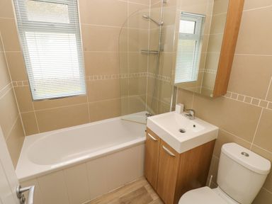 A bathroom with a bathtub a shower sink with cabinet mirror and toilet at Cwtch Lodge 42 Stepaside near Wisemans Bridge