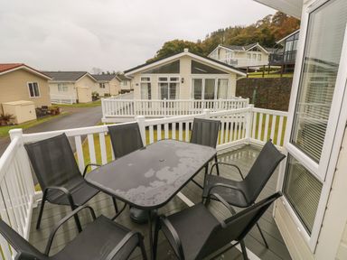 A patio with a black table and six black chairs surrounded by white railing outside a house at Cwtch Lodge 42 Stepaside near Wisemans Bridge