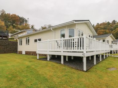 A modular home with a white deck and railing on a grassy lawn at Cwtch Lodge 42 in Stepaside near Wisemans Bridge