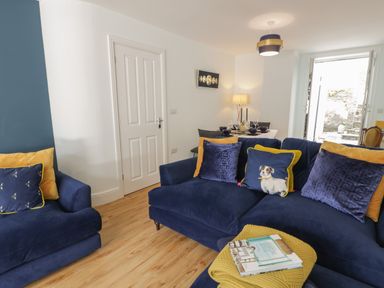 A living room with blue sofas and yellow cushions next to a dining table set at Bryn Derfel in Borth-y-Gest near Porthmadog