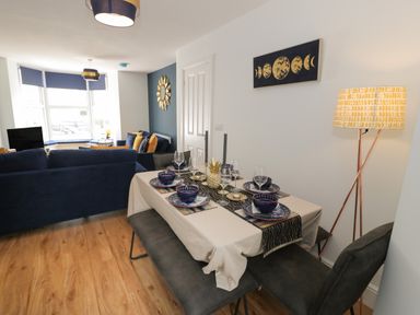 A dining table set with plates and glasses next to a living room with blue sofas at Bryn Derfel in Borth-y-Gest near Porthmadog