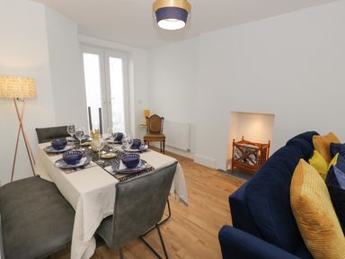 A dining area with a set table next to a sitting area with a blue sofa and yellow cushions at Bryn Derfel in Borth-y-Gest near Porthmadog