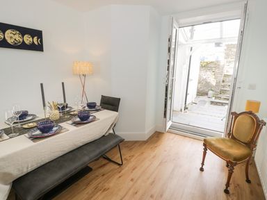 A dining room with a table set for four and a door open to an outdoor stone step area at Bryn Derfel in Borth-y-Gest near Porthmadog