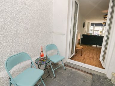 A small patio area with two blue chairs and a small round table with a bottle and glasses at Bryn Derfel in Borth-y-Gest near Porthmadog