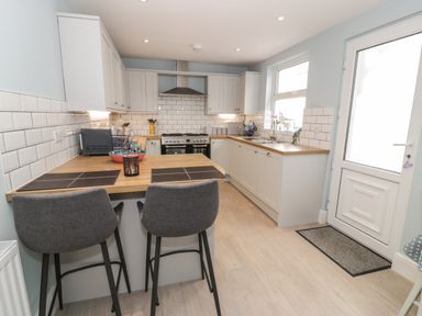 A kitchen with a wooden countertop two gray bar stools a stove and a white door at Bryn Derfel in Borth-y-Gest near Porthmadog