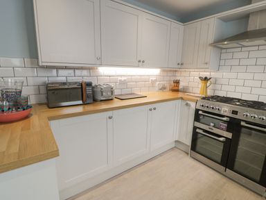 A kitchen with white cabinets wooden countertops a toaster microwave stove and cooking utensils at Bryn Derfel in Borth-y-Gest near Porthmadog
