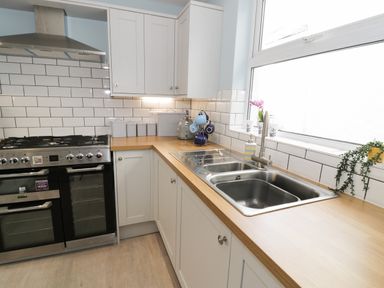 A kitchen with a stove, white cabinets, a double sink, wooden countertops, and a window with plants on the sill at Bryn Derfel in Borth-y-Gest near Porthmadog