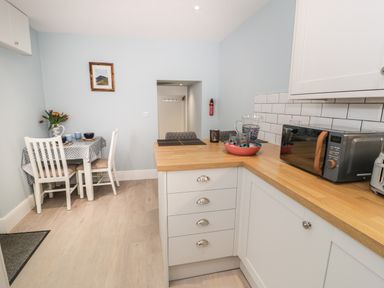 A kitchen with white cabinets wooden countertop microwave dining table with chairs and teapot with flowers at Bryn Derfel in Borth-y-Gest near Porthmadog