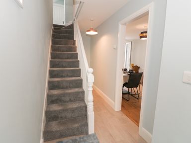 A hallway with carpeted stairs and a view into a dining room with chairs and a table at Bryn Derfel in Borth-y-Gest near Porthmadog
