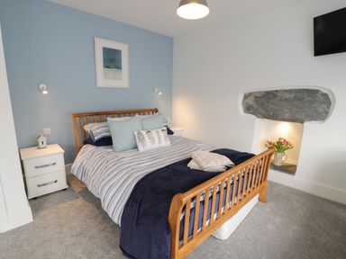 A bedroom with a wooden bed frame striped bedding and pillows beside white nightstands and a wall niche with flowers at Bryn Derfel in Borth-y-Gest near Porthmadog