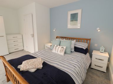 A bedroom with a wooden bed frame striped bedding bedside tables a chest of drawers and a blue accent wall at Bryn Derfel in Borth-y-Gest near Porthmadog
