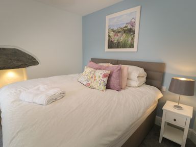 A bed with pillows and folded towels beside a nightstand with a lamp in a bedroom at Bryn Derfel in Borth-y-Gest near Porthmadog